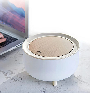 Small modern trash bin with simple half-spherical pot-like design made of white plastic with light wooden lid opening easily with push button and barely visible small legs 
