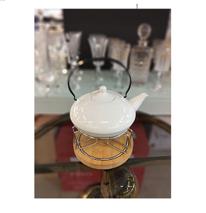 Glossy white porcelain teapot with low round base short spout and domed lid topped with small round handle features large curved black metal top handle for easy carrying and serving 
