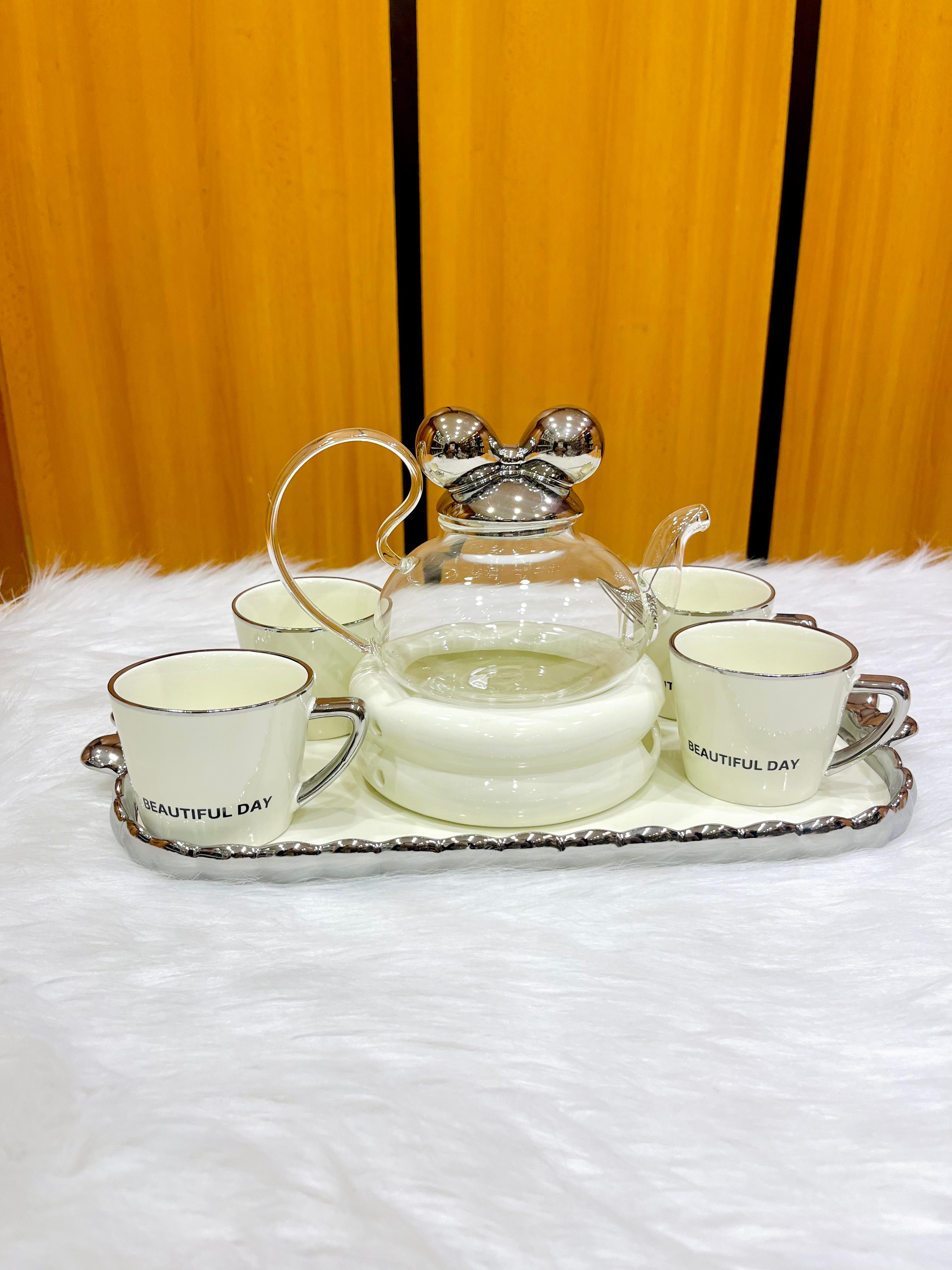 A tea set consisting of a crystal glass teapot, four white porcelain cups, and an ornate silver tray.